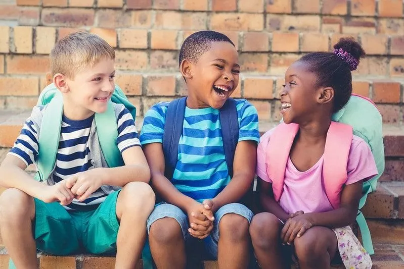 Three school kids sat by a wall laughing at shark jokes.