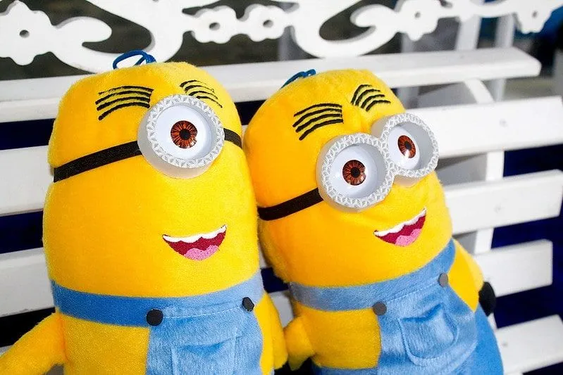 Two minion soft toys sat on a bench smiling into the distance.
