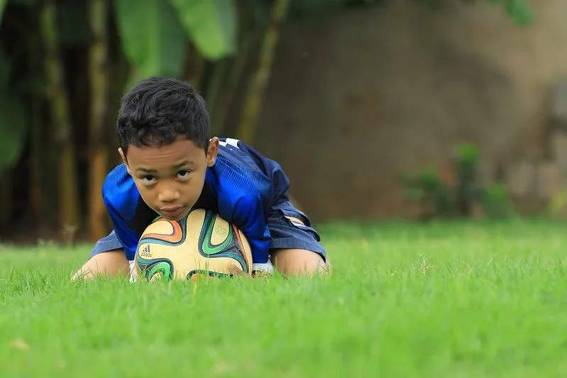 Young boy leaning on a football in the garden. 