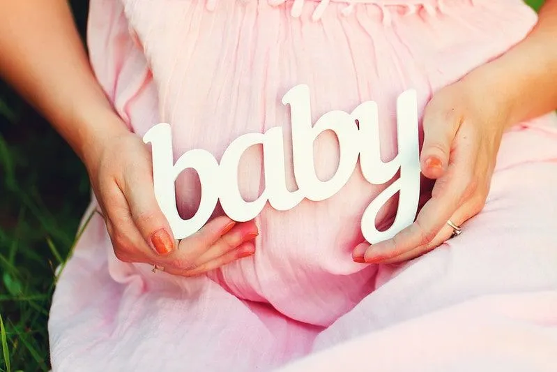 Mum-to-be wearing a pink dress holding the word baby over her bump.