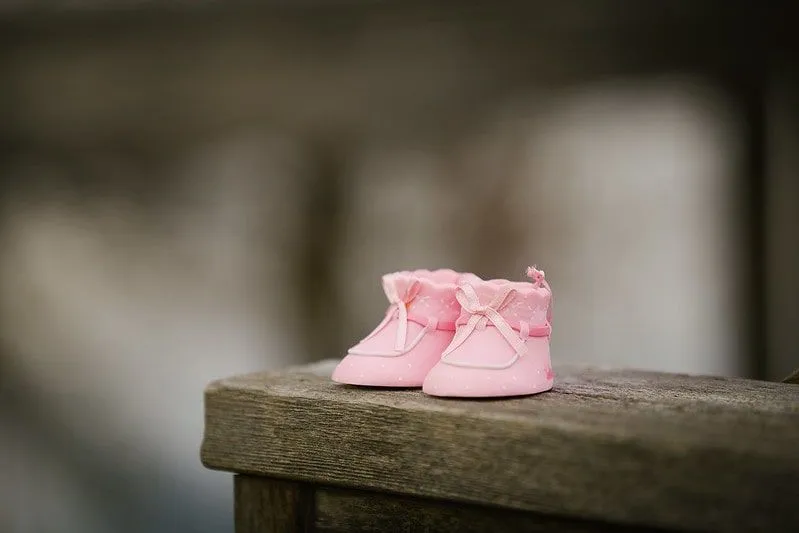 Little pink boots for a baby girl on a wooden wall.