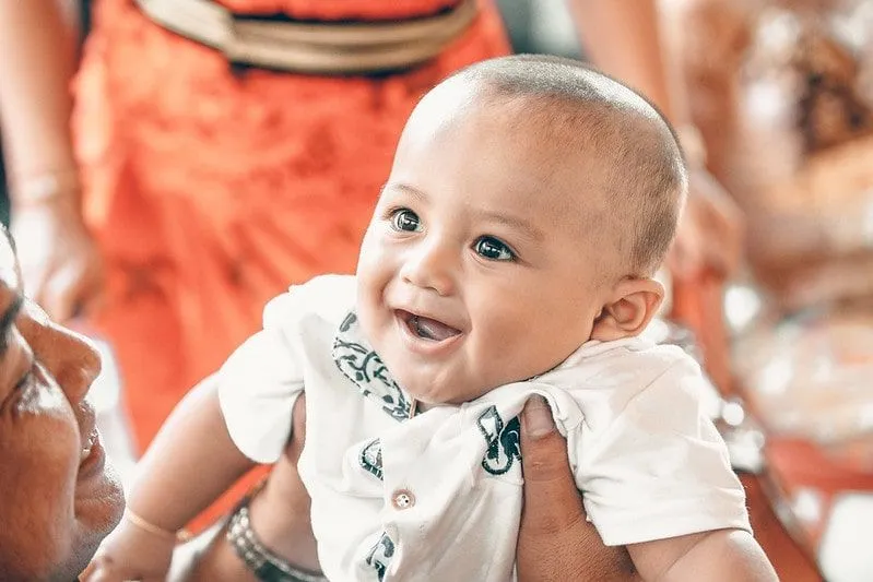 Baby boy in his family's arms, smiling back at them. 