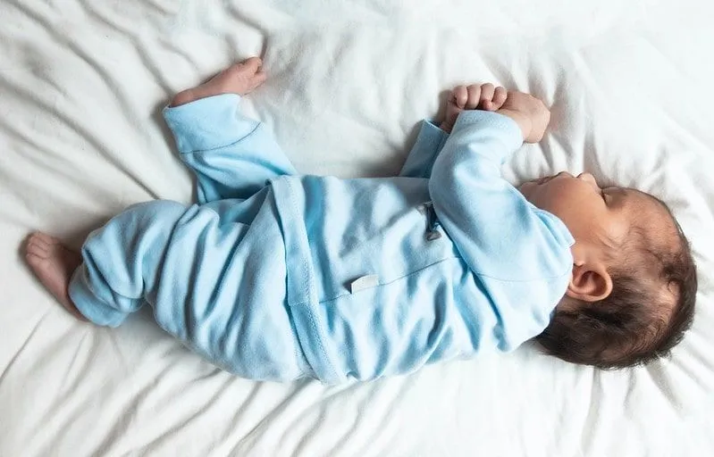 Baby boy wearing blue sweetly sleeping on the bed on his side.