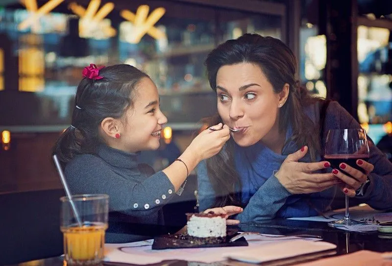 A young girl is feeding her mother cake at a restaurant.