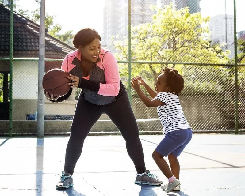 Mother and daughter smiling at each other while playing basketball.