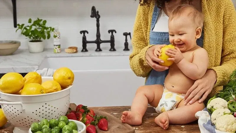 Baby sat on the kitchen worktop holding a lemon and smiling.
