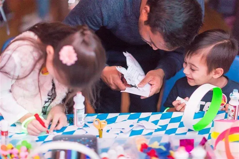 A dad helping two young siblings cut out their crafts.
