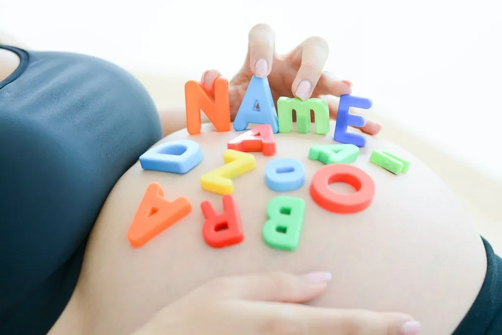 Expectant mother with letter blocks spelling out 'name' on her tummy.