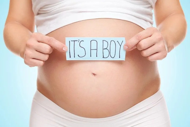Pregnant woman holding a sign reading 'it's a boy' in front of her bump.