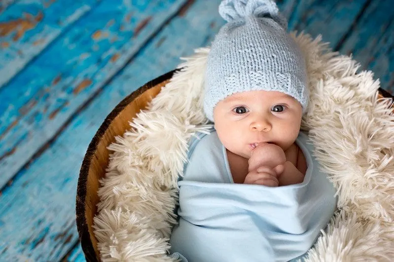 Baby born wearing blue woolly hat wrapped in blue on a fluffy blanket.