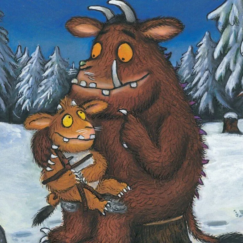 An adult Gruffalo sat on a tree stump in a snowy forest, with a young Gruffalo on his lap.