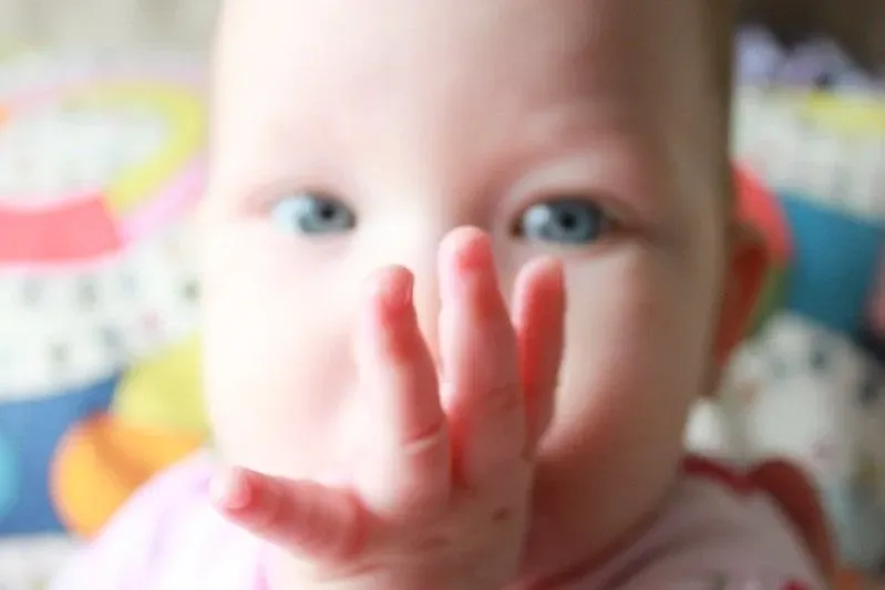 Blue-eyed baby with its thumb in its mouth.
