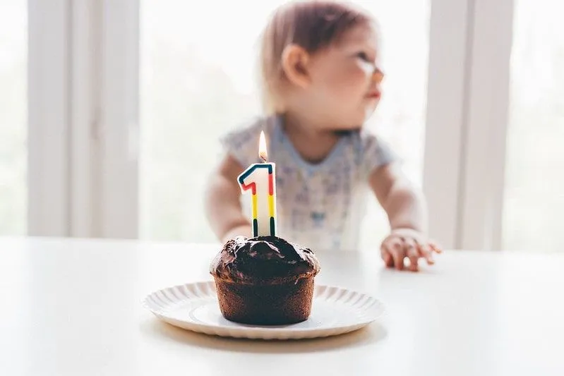 Birthday cake with a 1 candle lit in front of a toddler.