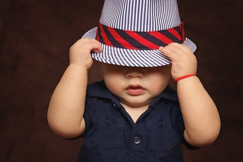 Baby boy wearing a striped fedora hat, pulling it over his eyes.
