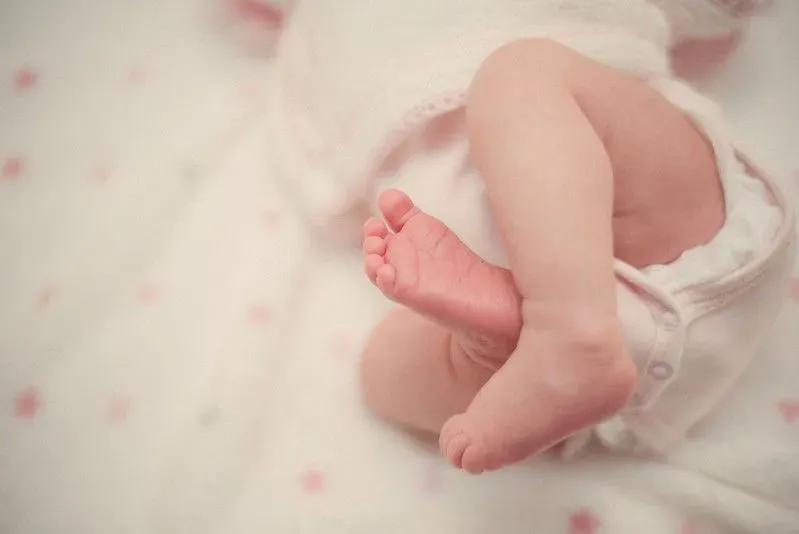 Newborn baby girl's legs and feet as she lies in the cot.