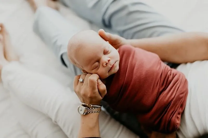 Newborn baby wrapped up in a blanket in its parent's arms.