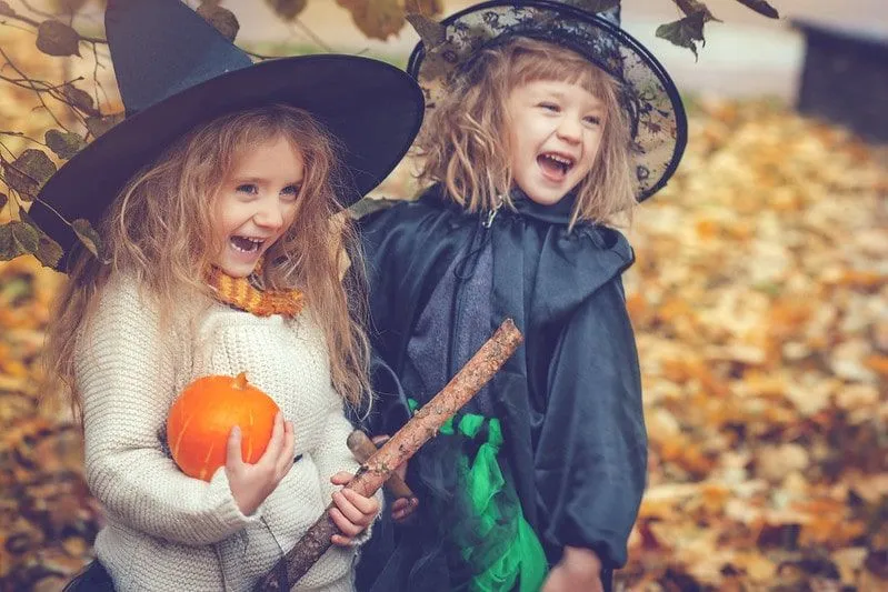 Two small girls in witch outfits laughing with a pumpkin.