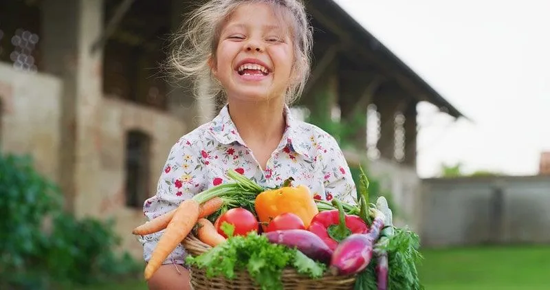 Little girl holding a basket of vegetables smiling.