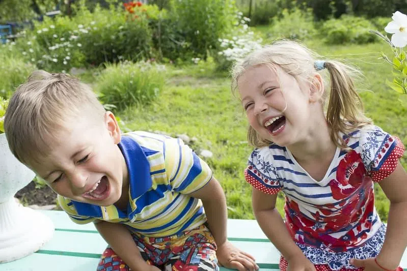 Little boy and girl sitting on a bench in the garden laughing.