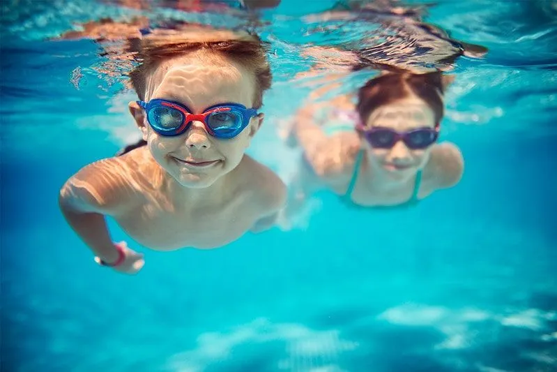Little boy and girl swimming in the pool underwater wearing goggles.