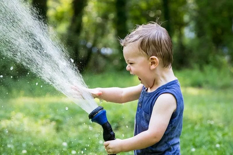 Little boy outdoors playing with the water hose.