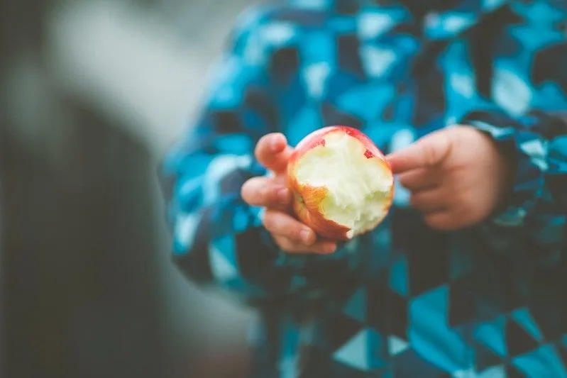 Little kid in a blue jacket holding a half-eaten apple.