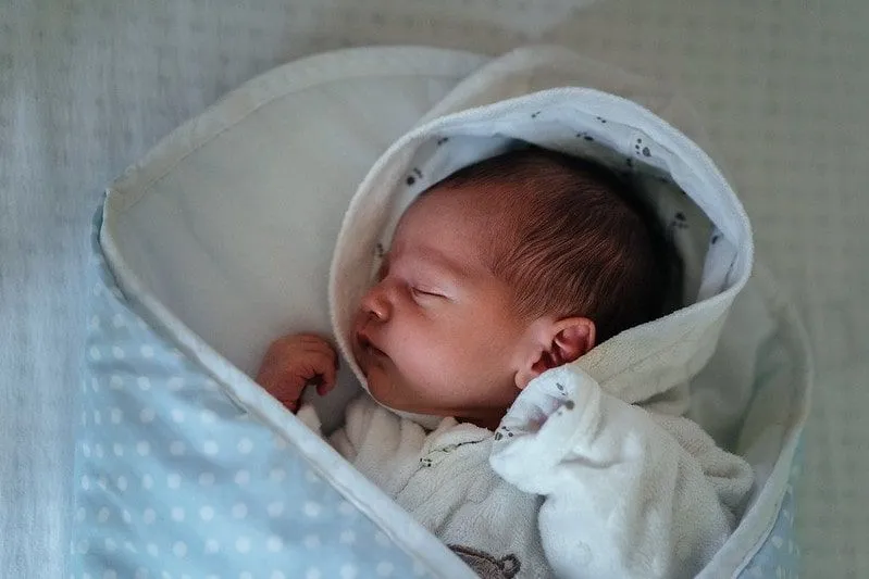 Newborn baby boy sleeping in a blue polka dot blanket.