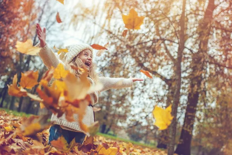 Happy girl smiling as she throws the autumn leaves up in the air.