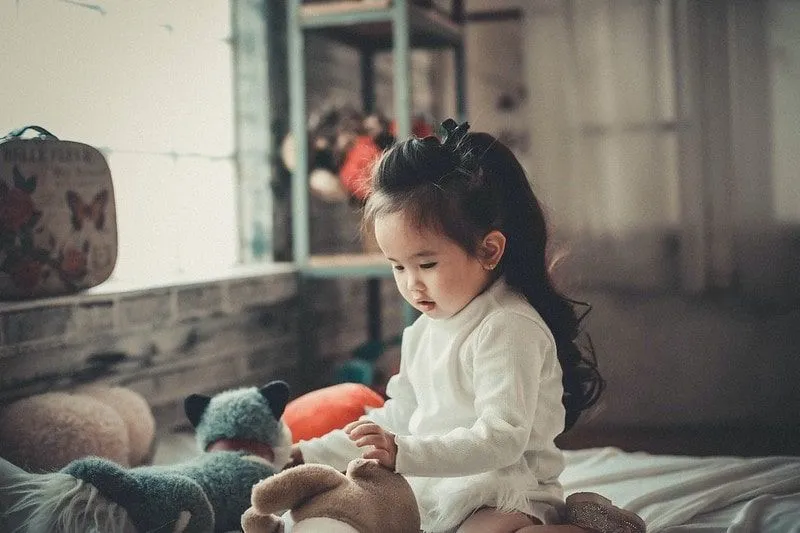Little girl with long hair playing with teddy bears.