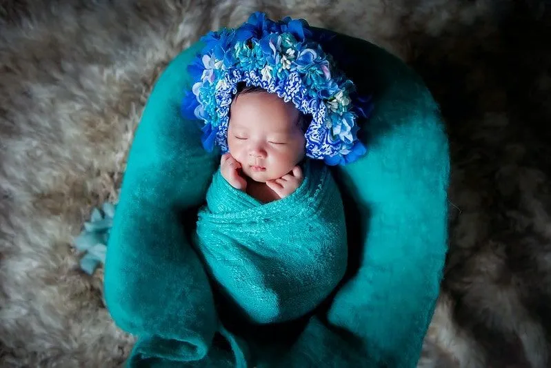 Baby wearing a blue flower crown sleeping in a turquoise blanket.