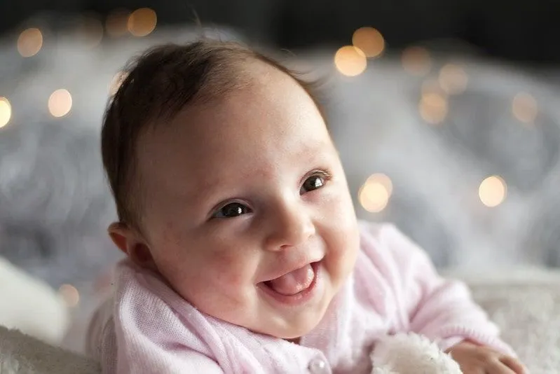 Baby girl in pink smiling and looking up at her parents. 