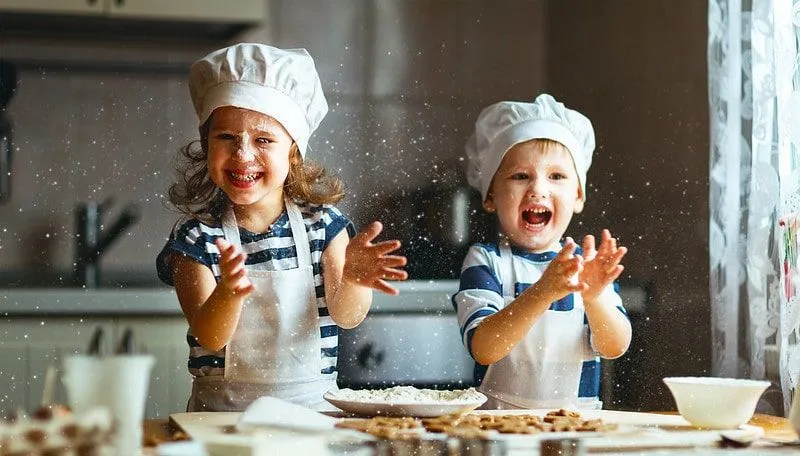 Little boy and girl wearing aprons and chef's hats playing with flour while baking cookies.