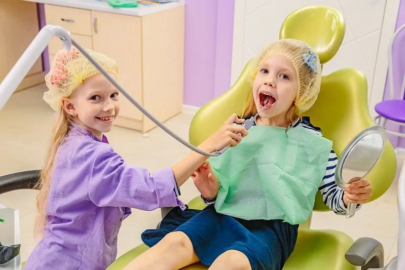 Two little girls playing dentist pretending to use the equipment on each other.