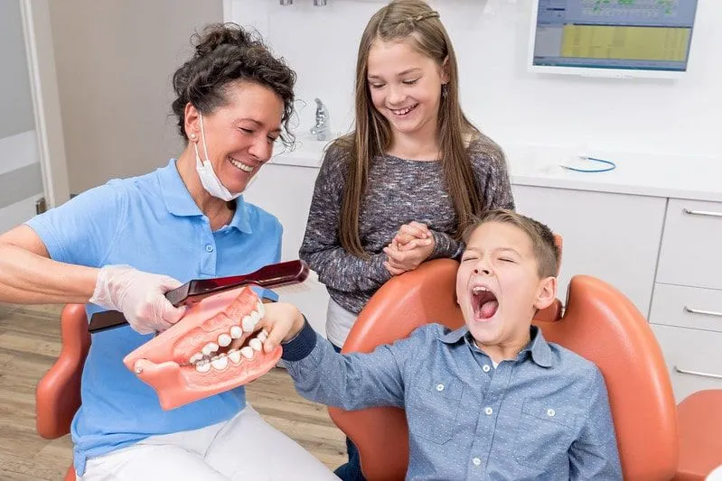 Kids joking around with the dentist, pretending to trap the boy's fingers in giant fake teeth.