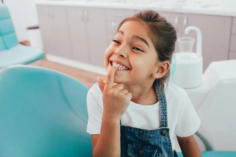 Young girl at the dentist smiling and pointing to her teeth.