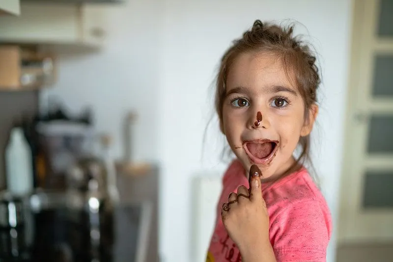 Little girl eating melted chocolate from her finger and has chocolate on her mouth and nose.