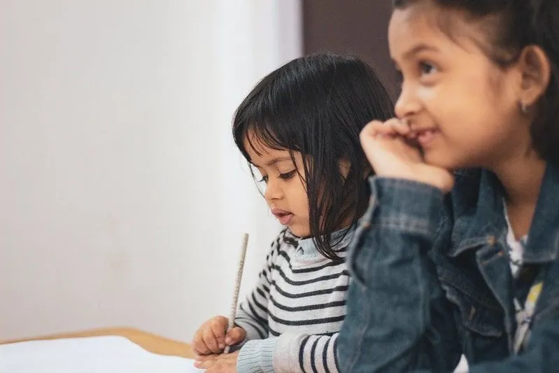 Two young girls sat at a desk learning and writing notes in the classroom.