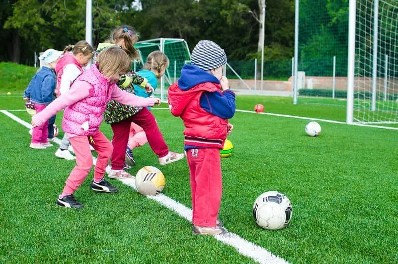 Small children outside kicking footballs during a PE lesson.