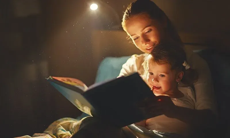Mum sat in bed with her daughter reading to her from a book.