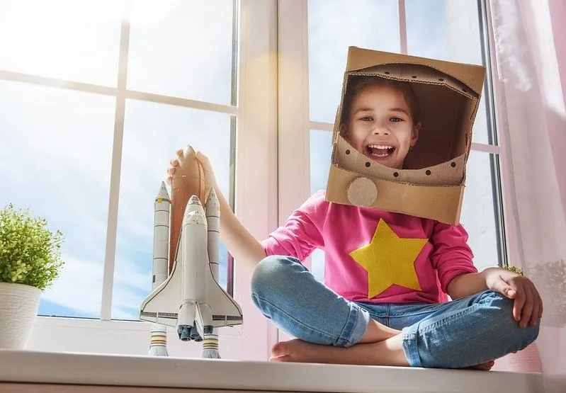 Girl in a homemade astronaut costume smiling as she hold a toy rocket.