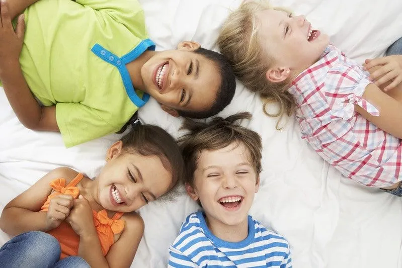 Four kids lying on a bed laughing at Spiderman jokes.