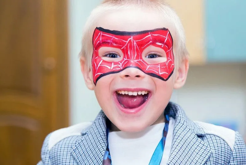 Boy with Spiderman mask face paint smiling happily.