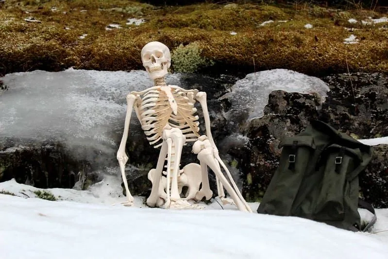 A funny skeleton sat in the snow leaning against some rocks.