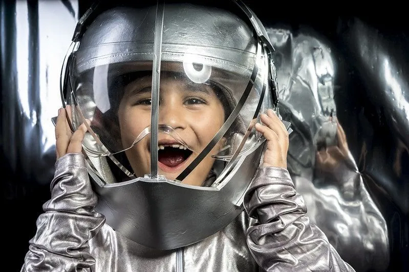 Little boy smiling wearing a silver astronaut suit and helmet.