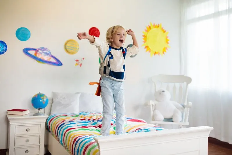 Boy in astronaut clothing standing on the bed in his space-themed room.