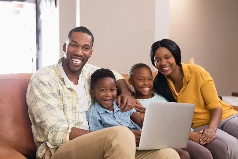 Family at on the sofa together laughing as they look up Monday jokes on the laptop.