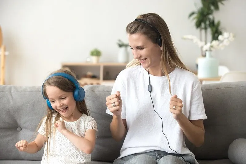 Mum and daughter sat on the sofa each listening to headphones to learn phonics.