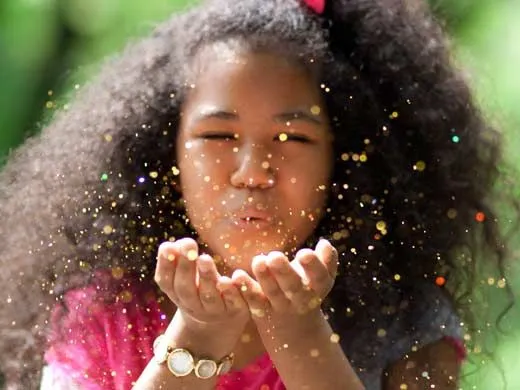 Little girl with her eyes closed blowing gold fairy dust out her hands.