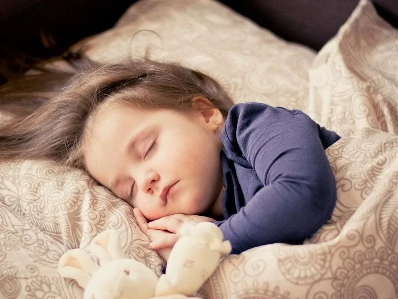Little girl sleeping in her bed with a bunny teddy, waiting for the tooth fairy.