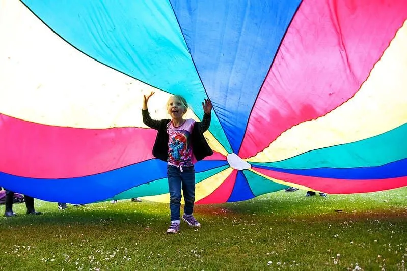 Young girl running under a colourful parachute playing games.